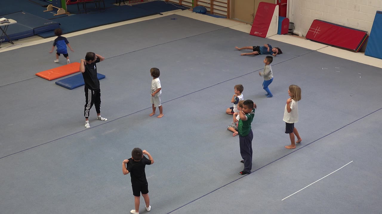 Children move around while an instructor stands on the gym floor.