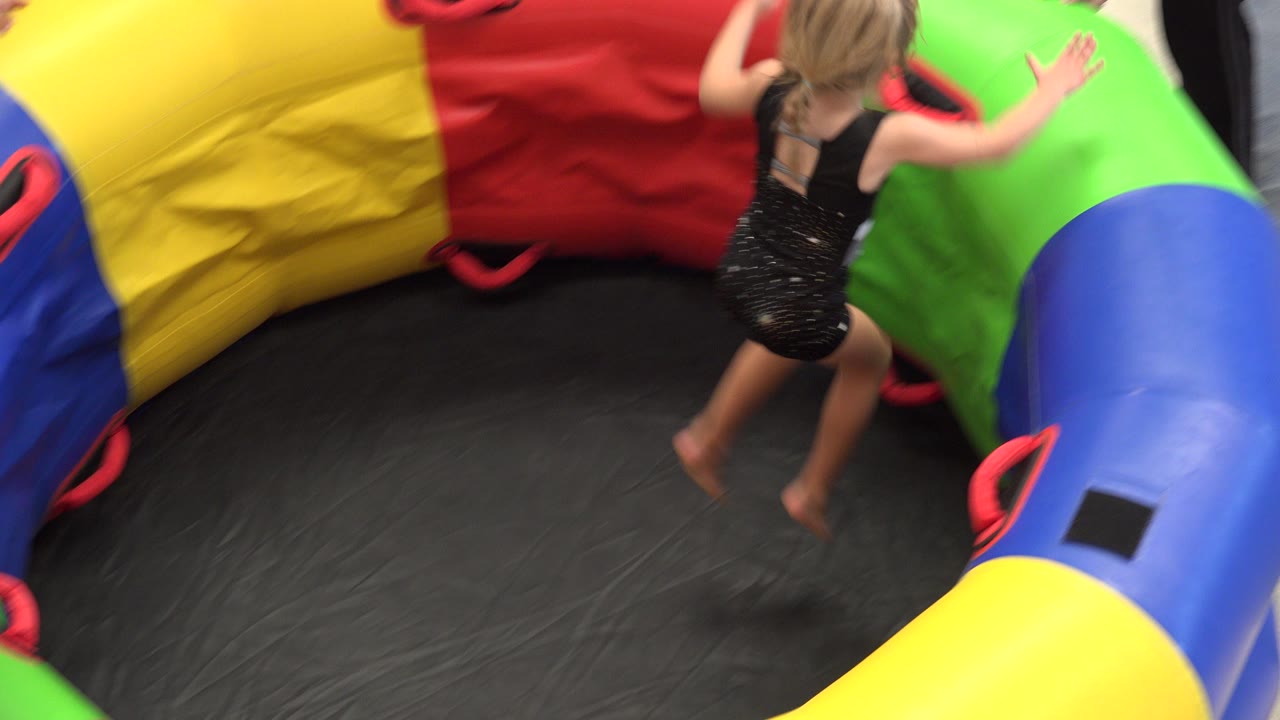 Blonde child jumping inside a colorful inflatable play area.