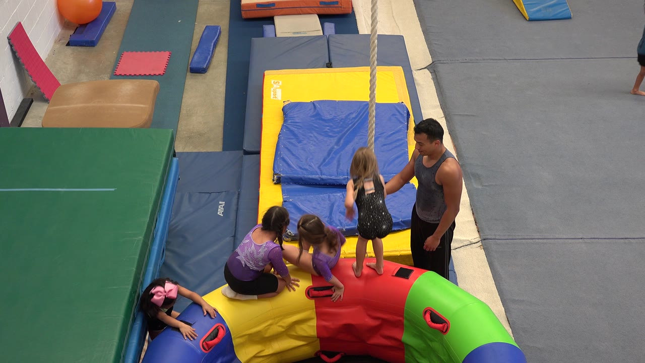 Children and an instructor beside a rope over padded gym mats.
