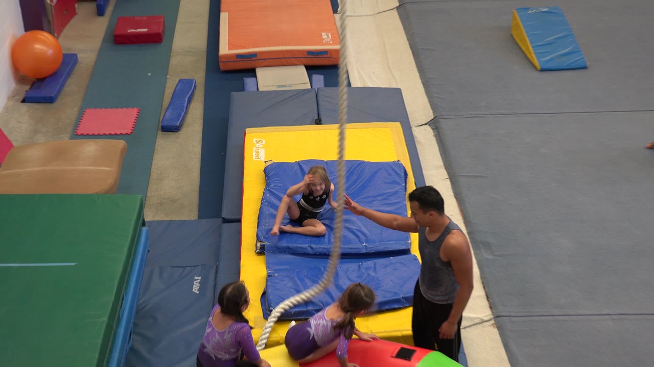 Girls and an instructor beside blue and yellow gymnastics mats.