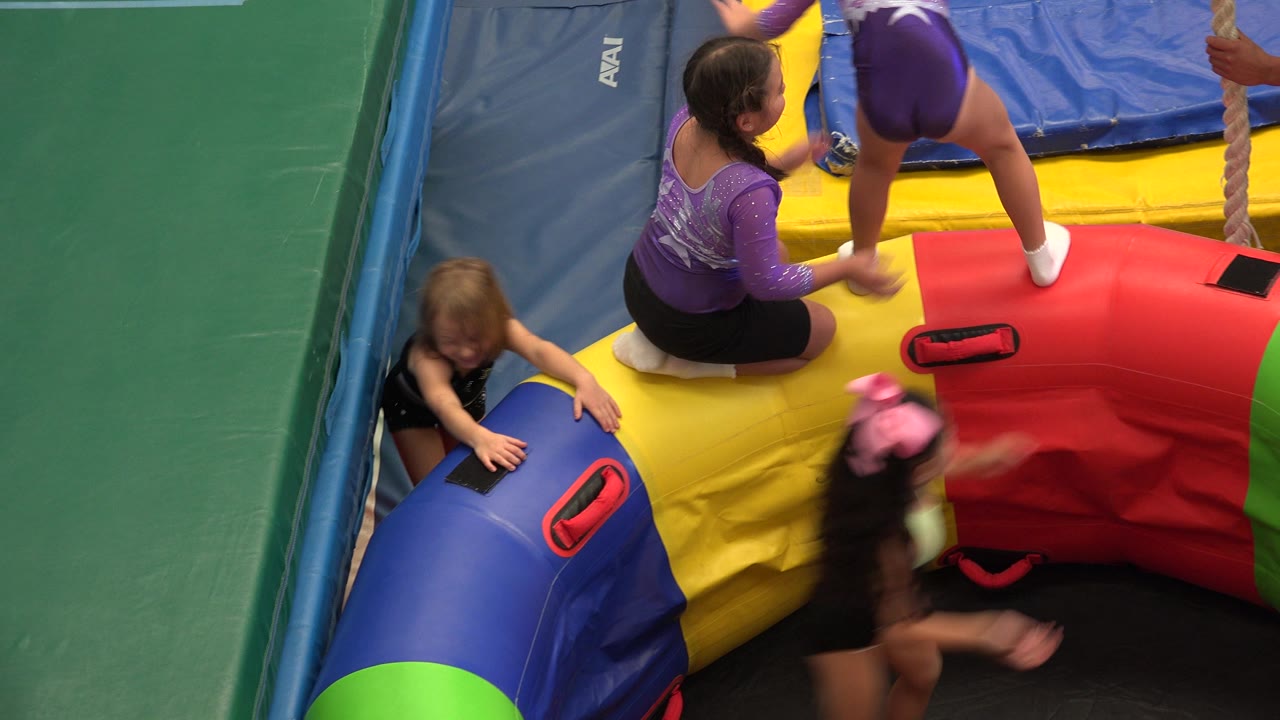 Children on colorful inflatable play equipment beside padded mats.