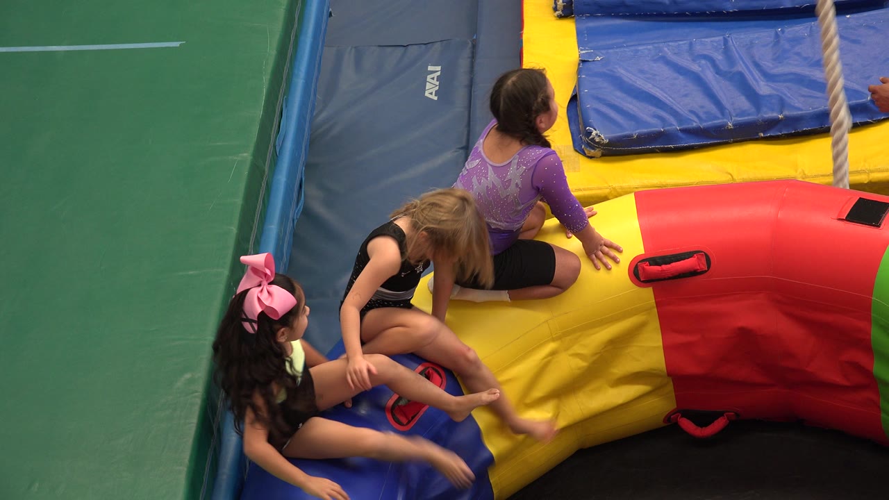Three young girls continue playing on the colorful inflatable, with blue crash mats and green wall padding visible around them in Cabo San Lucas, Mexico.