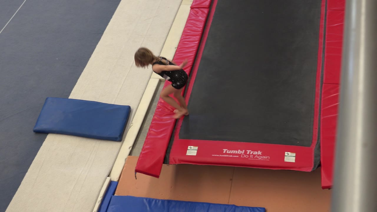 In Cabo San Lucas, Mexico, the young gymnast steps along the red border of the trampoline next to the white runway and blue mat.