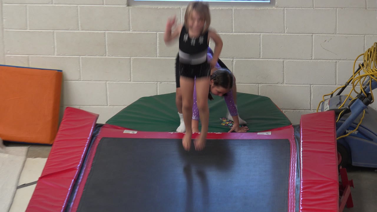 Child jumping on a red trampoline while another child waits behind her.