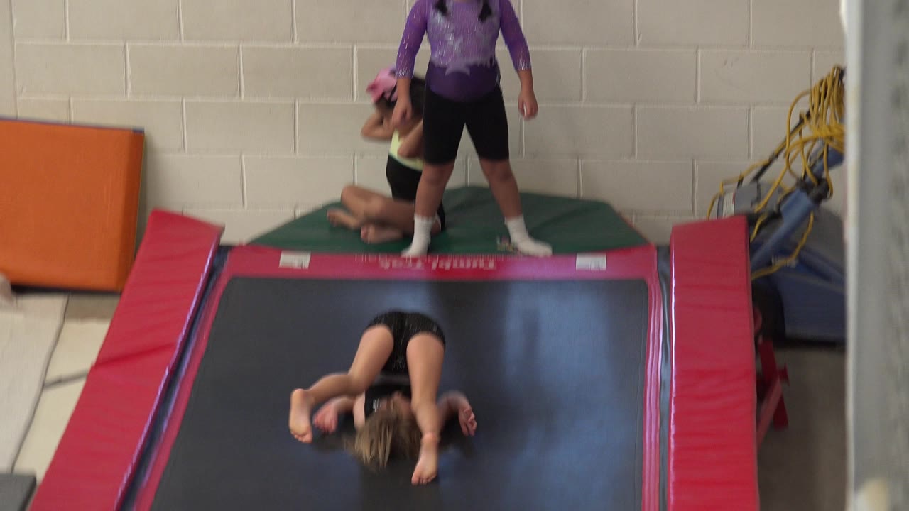 Girl lying on a trampoline while an adult stands near gym mats.