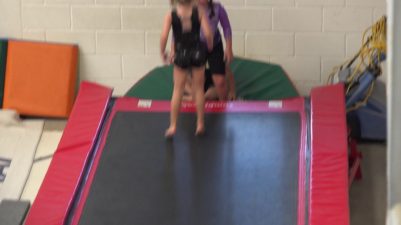 Two children on a trampoline in an indoor gym.