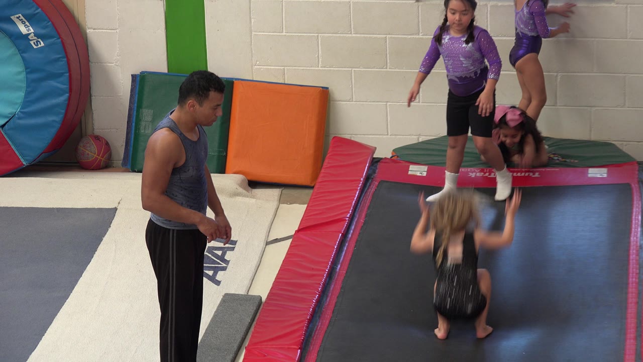 Coach watches children on a padded gymnastics trampoline lane.