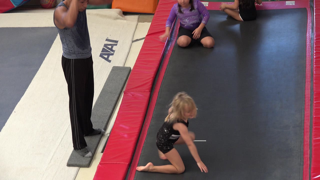 Children and an adult beside an indoor gymnastics trampoline platform.