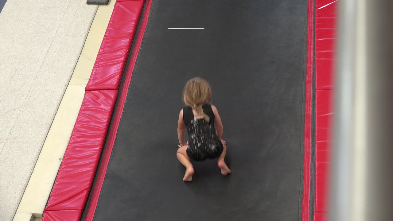 A high-angle view shows the girl still crouched near the center of the black trampoline in Cabo San Lucas, Mexico.