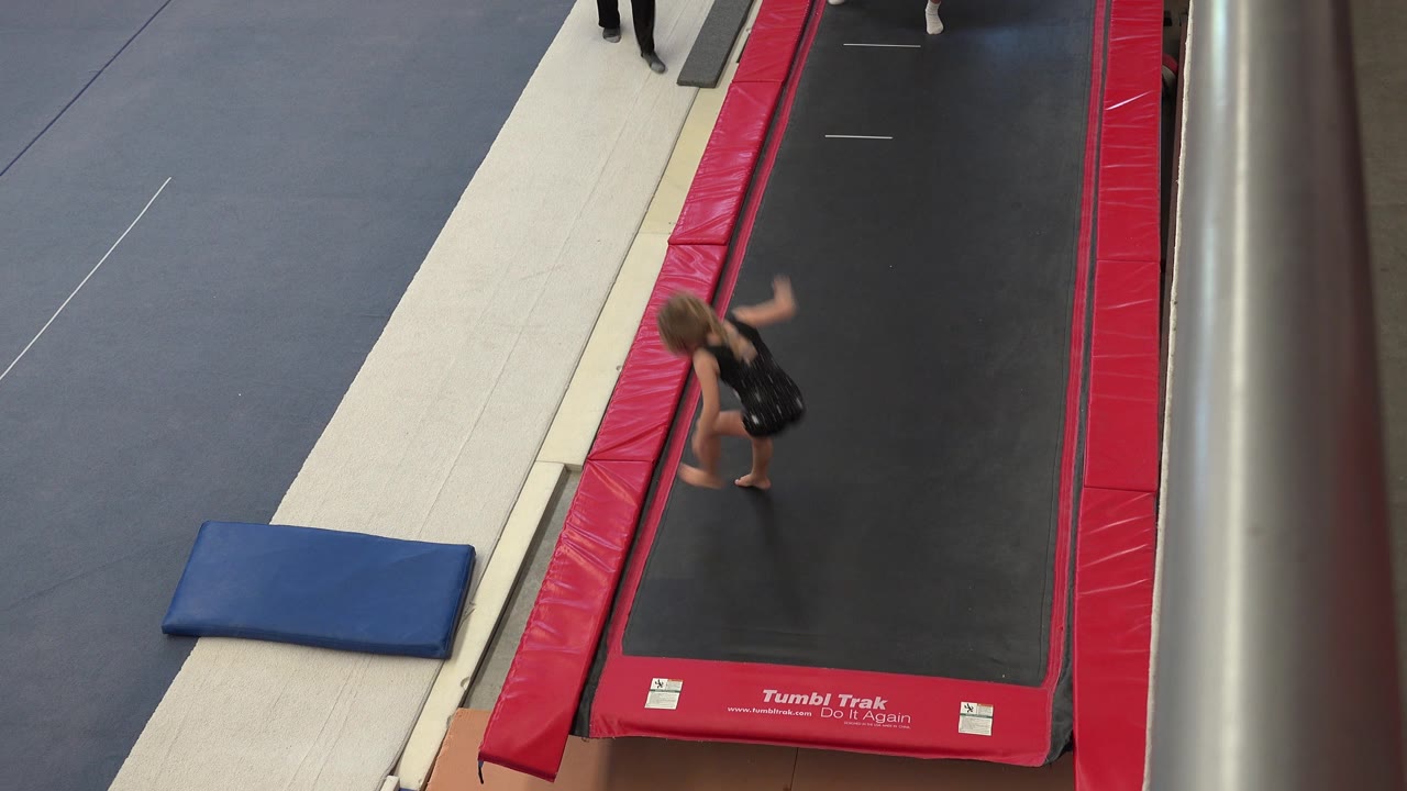 Child gymnast beside a red trampoline lane in a gym.