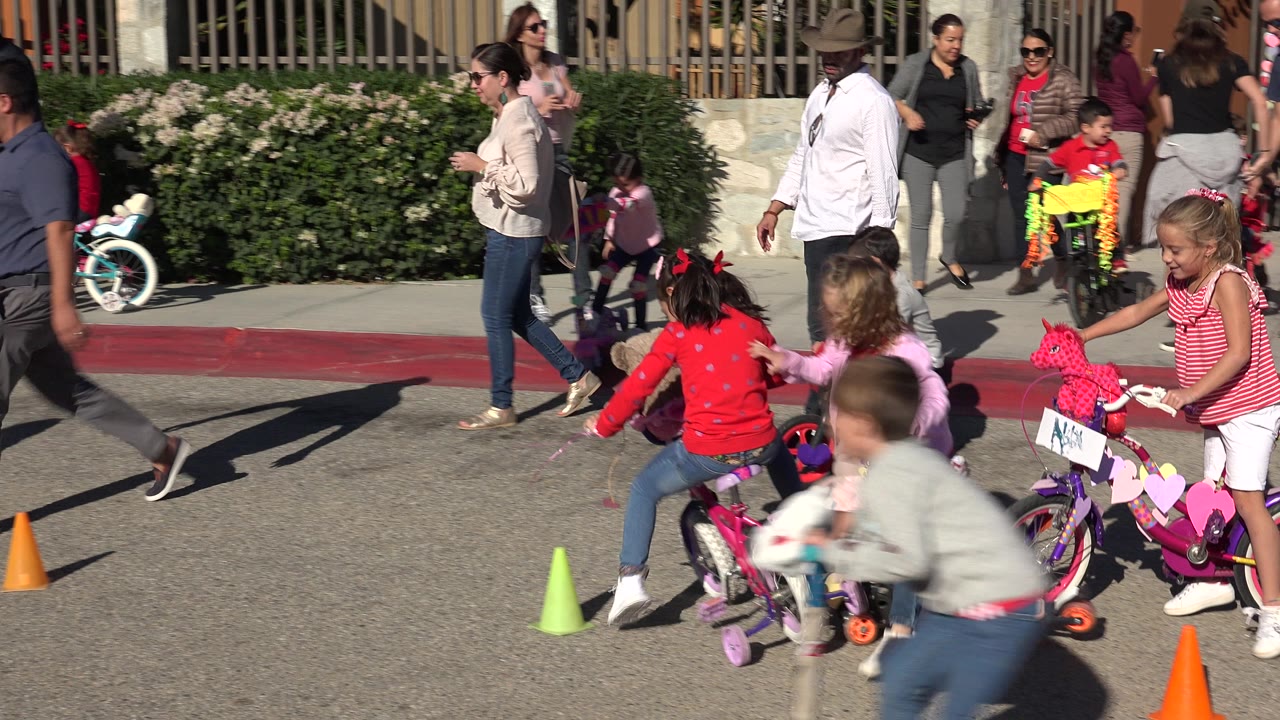 Children riding bikes and scooters near traffic cones on a sunny street.