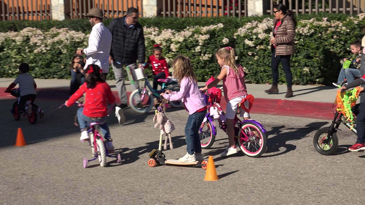 Children on bikes pass adults and cones on a paved street.