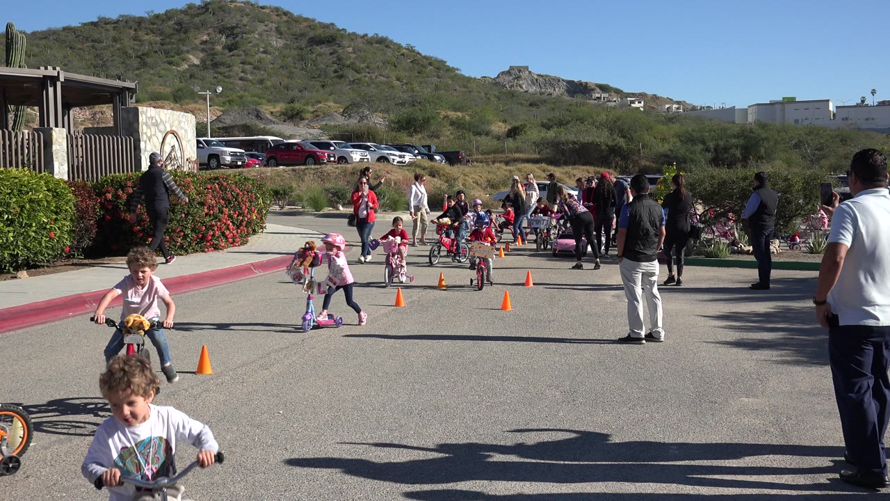 One second in, the Cabo San Lucas scene shows a girl on a scooter and another child on a small bike moving toward cones while a group of adults watches behind them.