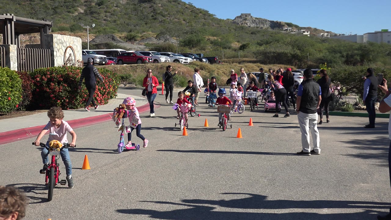 A child on a red bicycle rides near cones with other children behind.