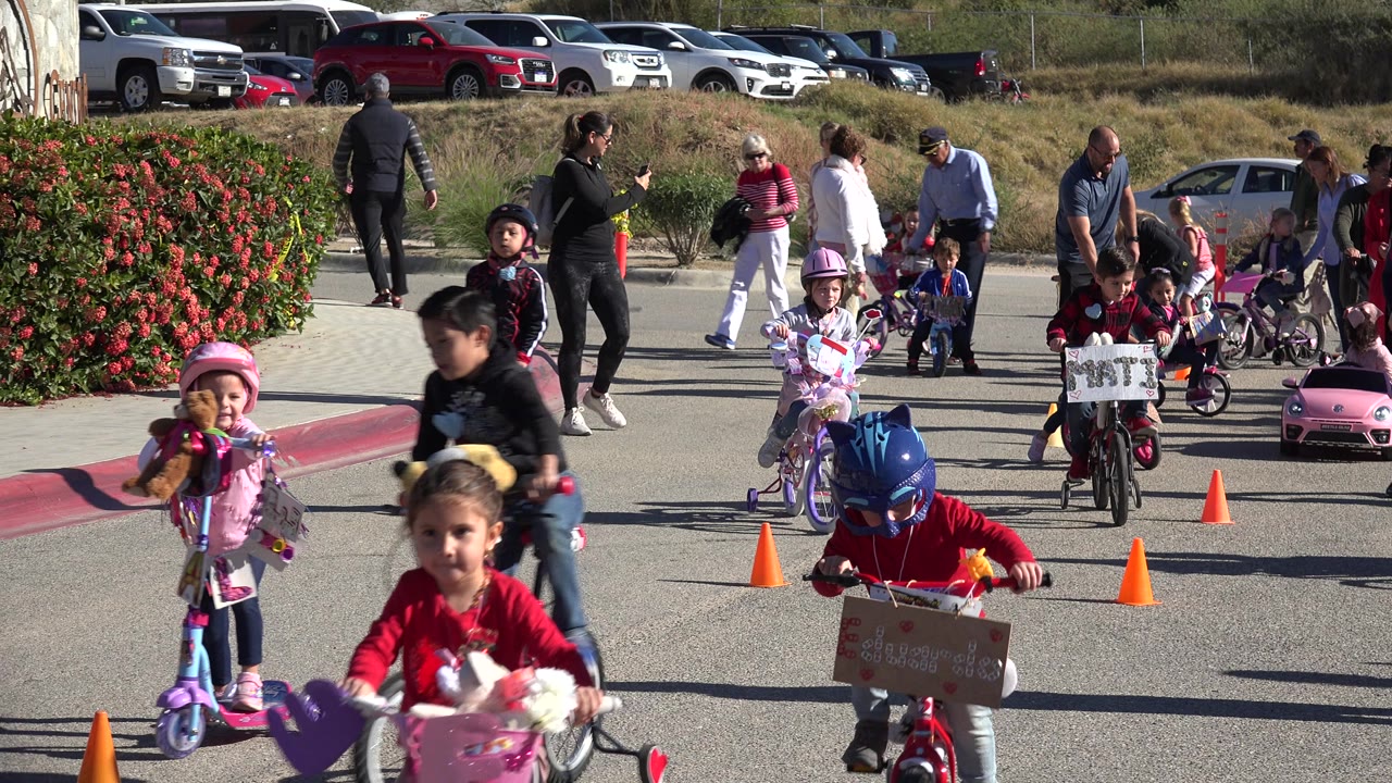 A girl on a pink scooter, a child on a small bike, and other children move through the cone course as adults stand in the sun in Cabo San Lucas, Mexico.