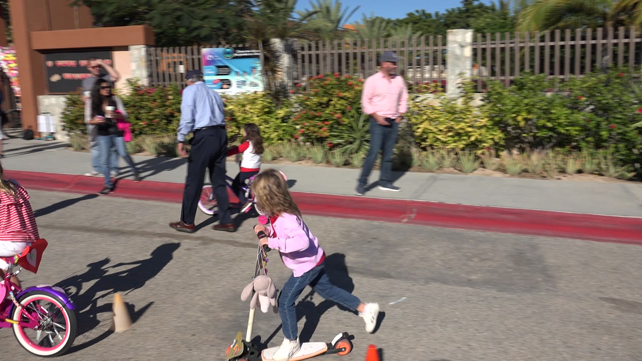 A child on a pink bicycle and a child on a scooter ride near a building entrance.