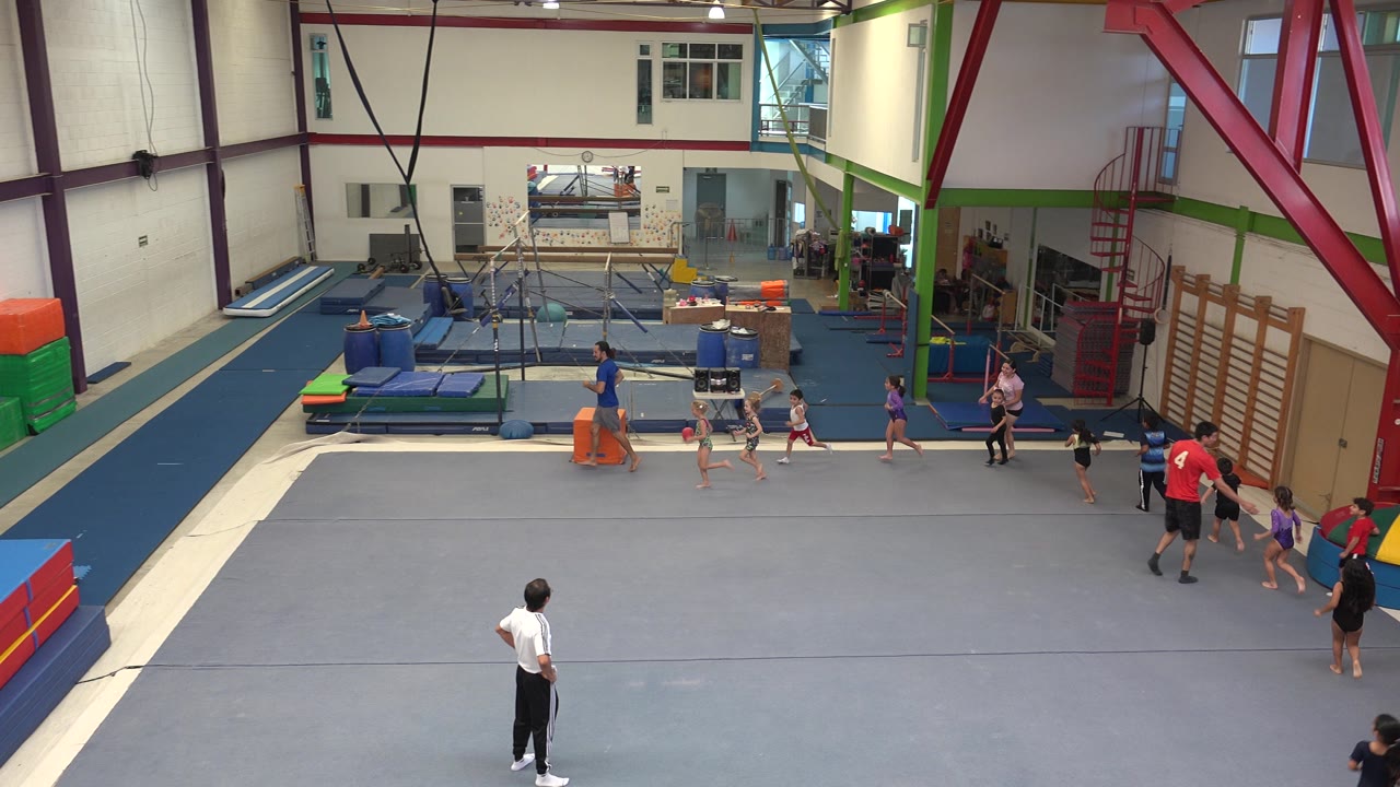 Kids and adults gather near the right side of an indoor gym.