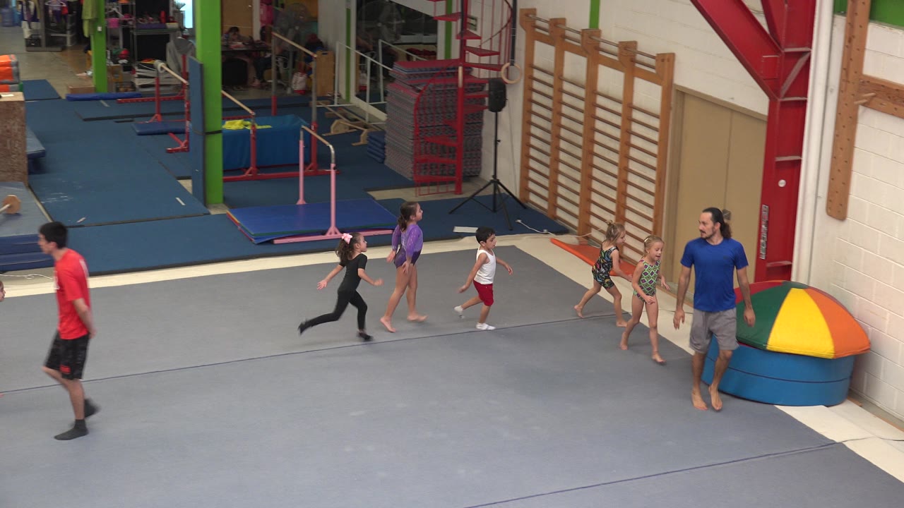 Children run in a line behind an adult instructor inside a gym.