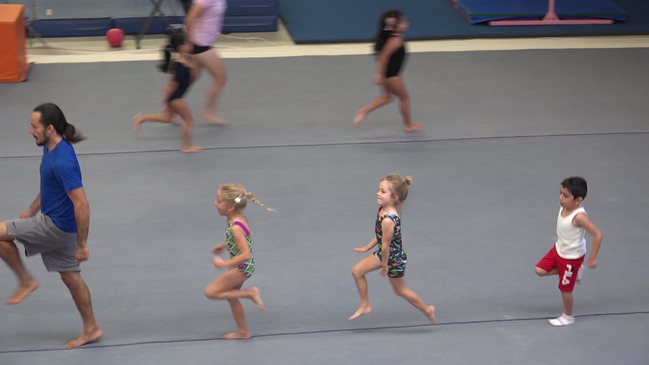 At 0:01 in Cabo San Lucas, Mexico, two girls in patterned leotards and a boy in red shorts run across the mat as the instructor moves at the edge of the frame.