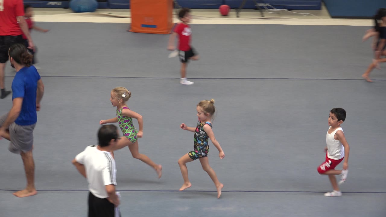 Children run past adults on a gym mat during class.