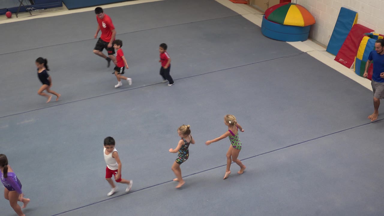 Children and coaches moving across a padded gymnastics floor.