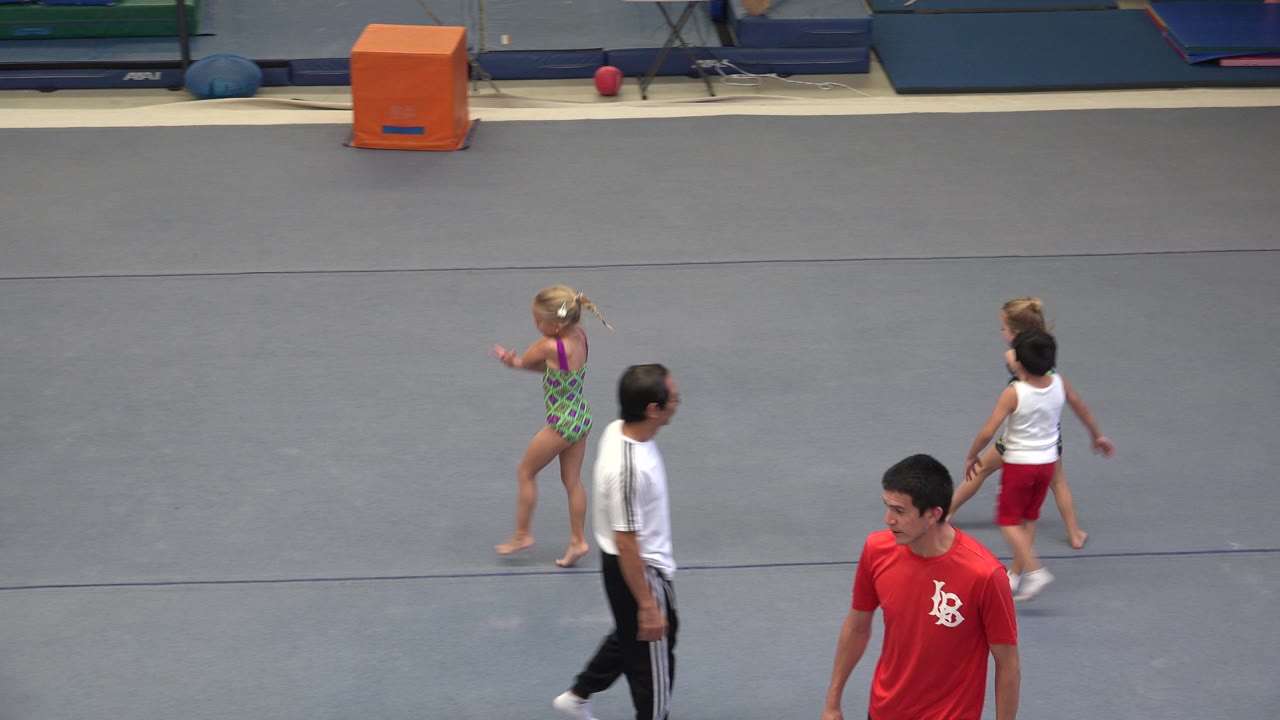 Children cross the gray gym floor with men in the foreground.