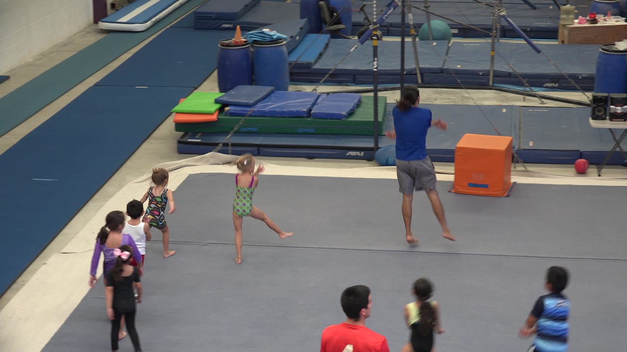 Children move across the gym while an instructor gestures ahead.