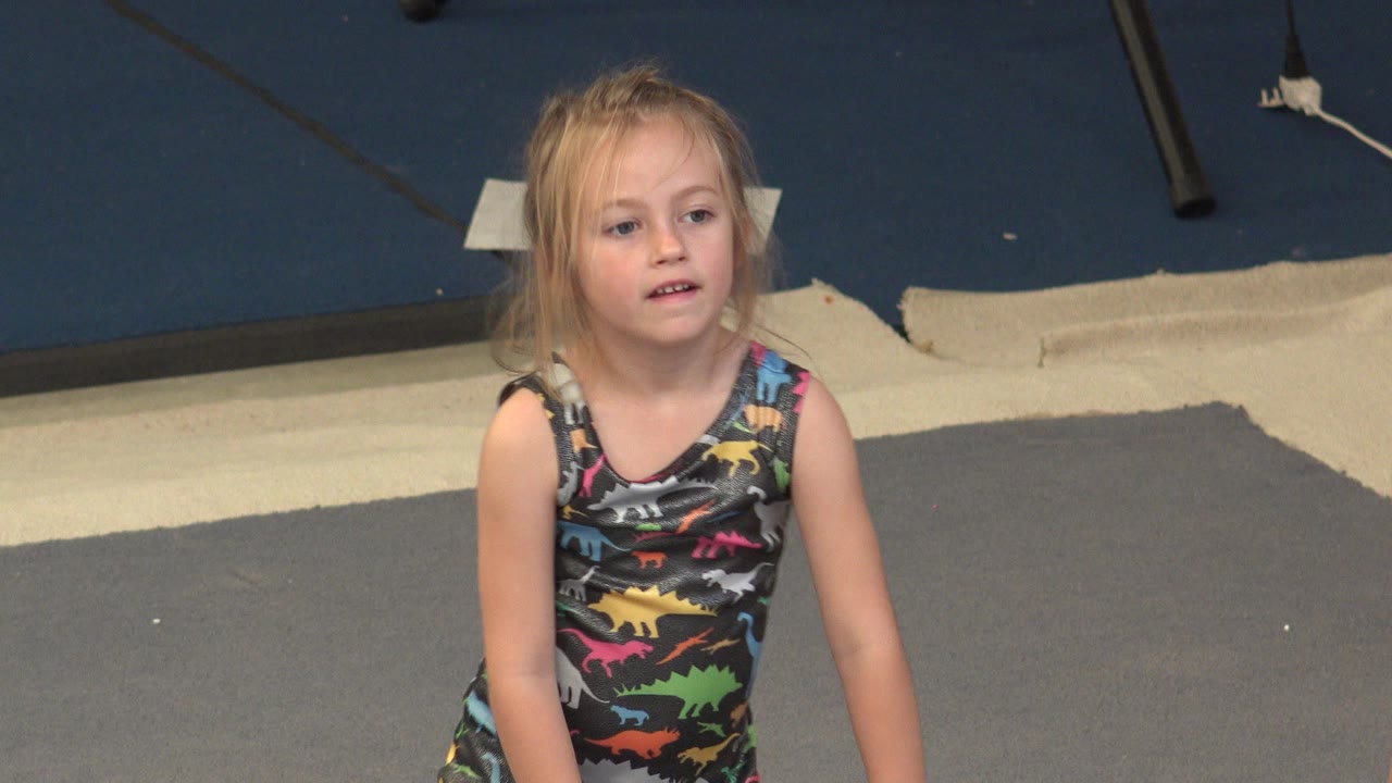 Young blonde girl facing camera on gray flooring near blue and cream mats.