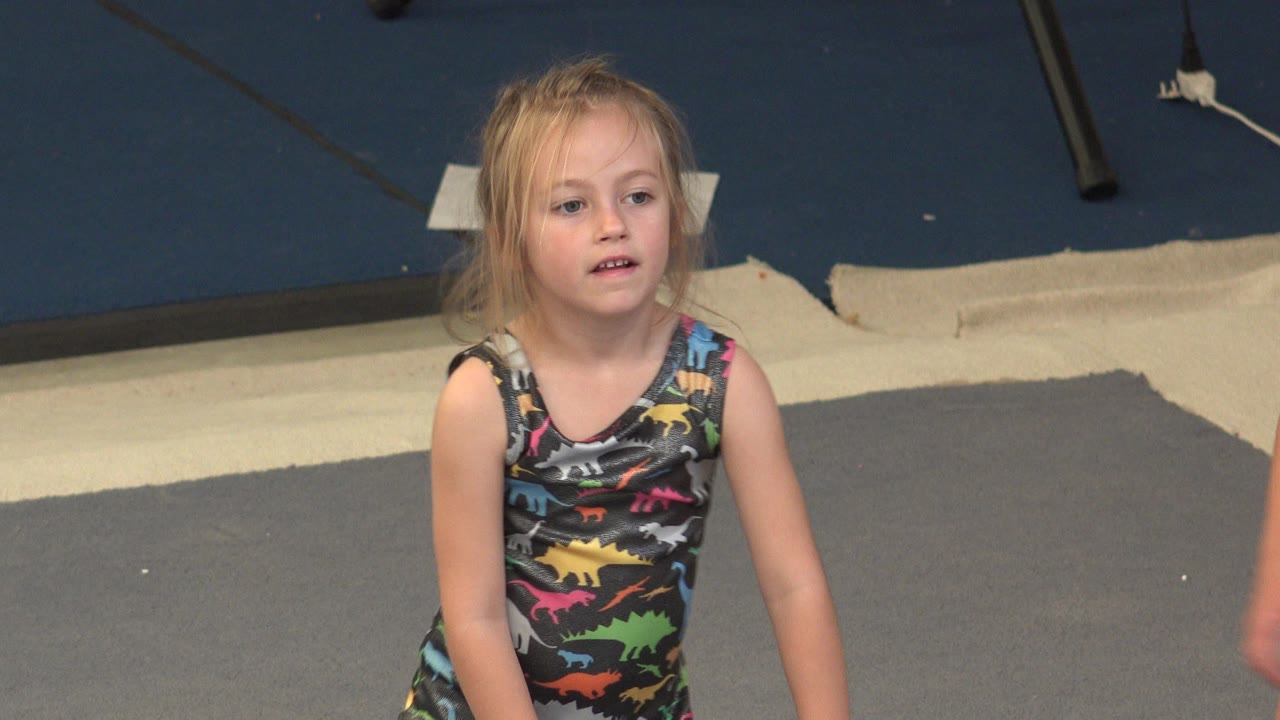 The girl remains centered and looking forward in the Cabo San Lucas clip, while a partial adult arm enters along the right edge near the exercise mats.
