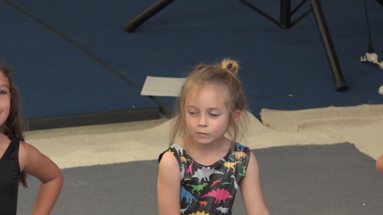 At 0:01 in Cabo San Lucas, Mexico, the blonde child looks downward in the center of the frame, with a dark blue mat and a second child cropped at the right edge.