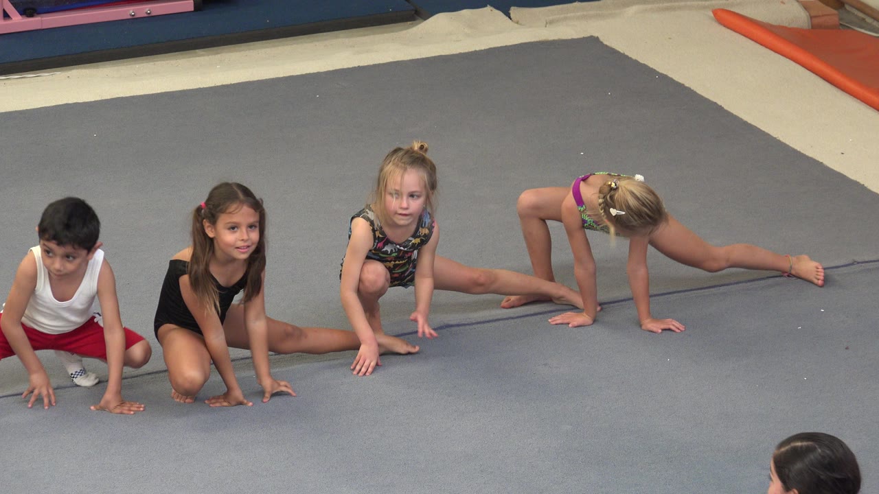 Children crouch and stretch on a gray gymnastics mat.