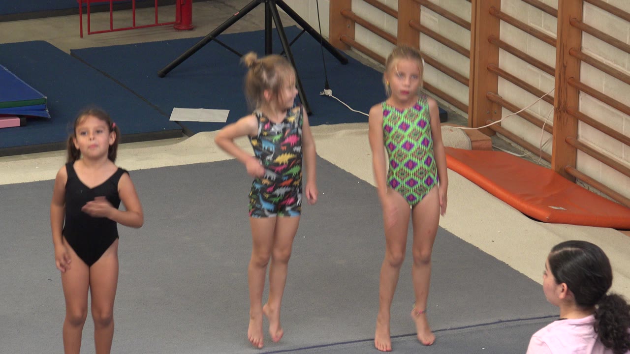 Three young girls standing on a gym mat during gymnastics.