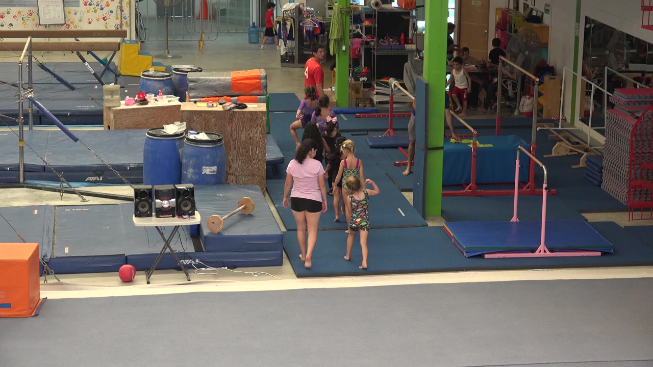 Gymnastics practice floor with adults, children, and uneven bars.