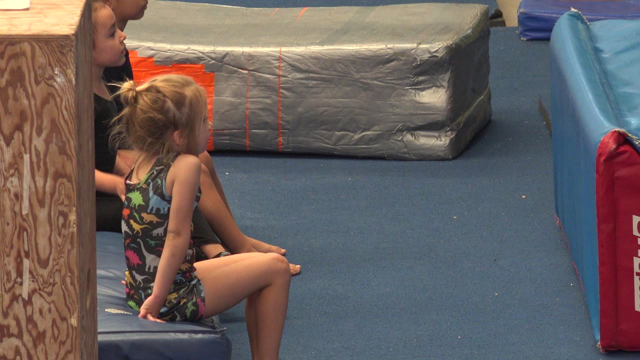 Young child seated on a gym mat beside an adult instructor.