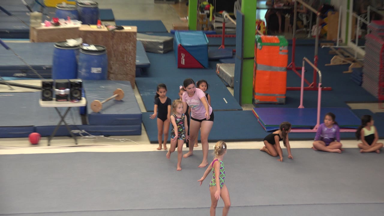 A line of young girls continues across the gray floor while other children sit near blue mats and colorful gym padding inside the Cabo San Lucas sports academy.