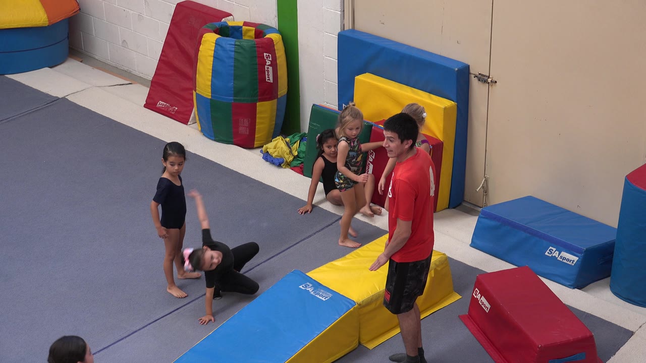 Child on the mat with instructor and other children nearby.
