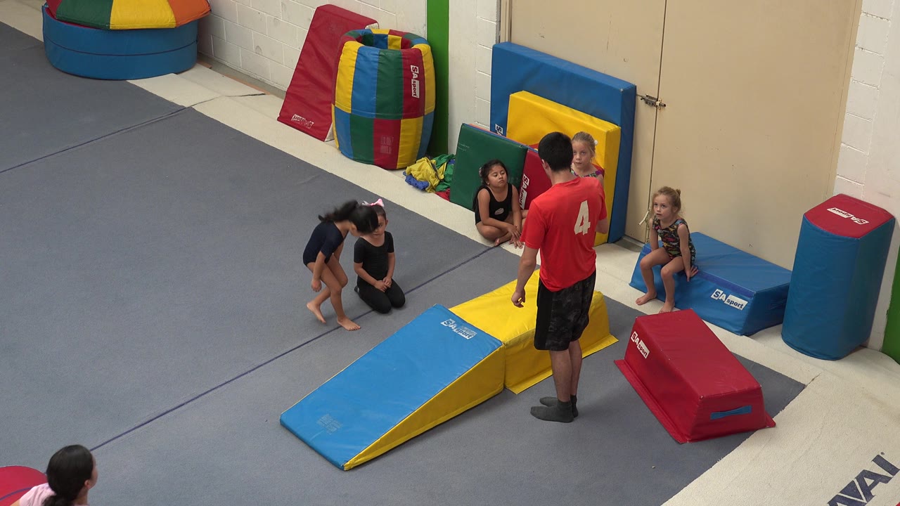 Coach standing near children and foam play ramps in a padded activity area.