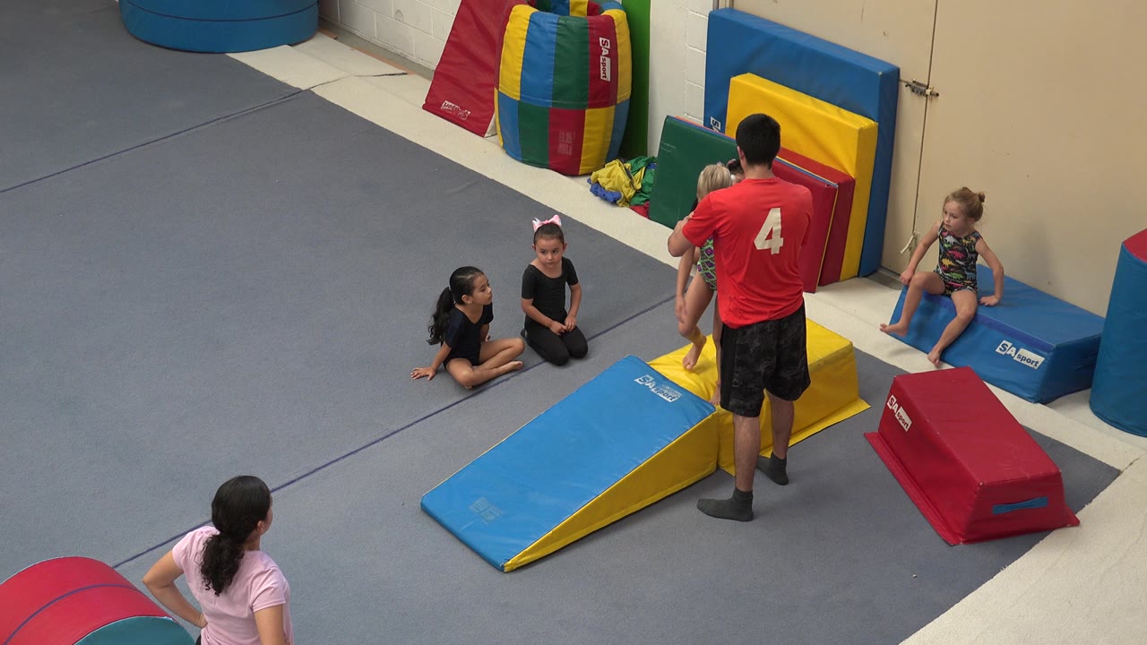 In Cabo San Lucas, the instructor remains centered with his back to camera as children sit and wait around the wedge mat and soft gym blocks.