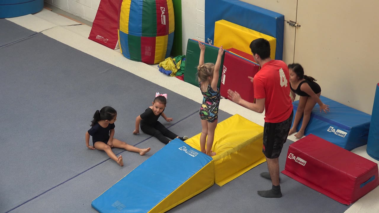 Child stands on a yellow mat as instructor holds a red pad.