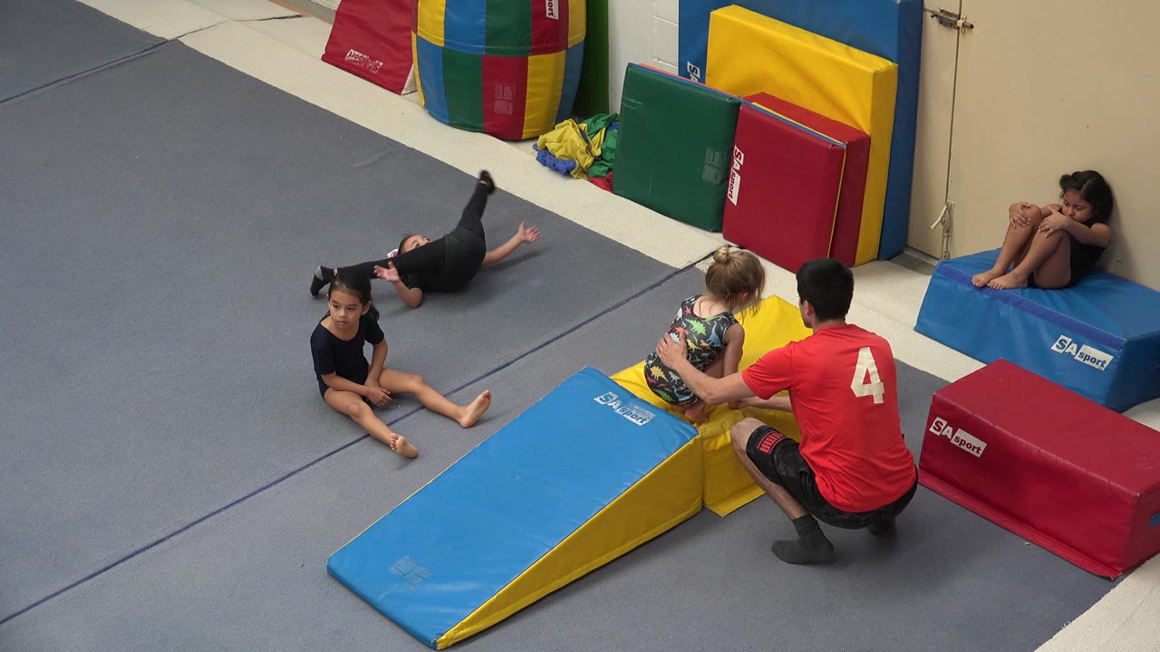 Children and an instructor gather around padded gymnastics mats.