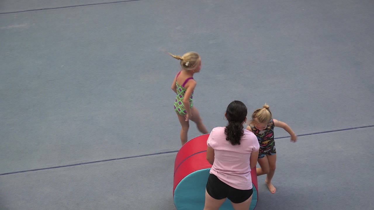 Adult woman helps two young girls beside a red and teal foam barrel.