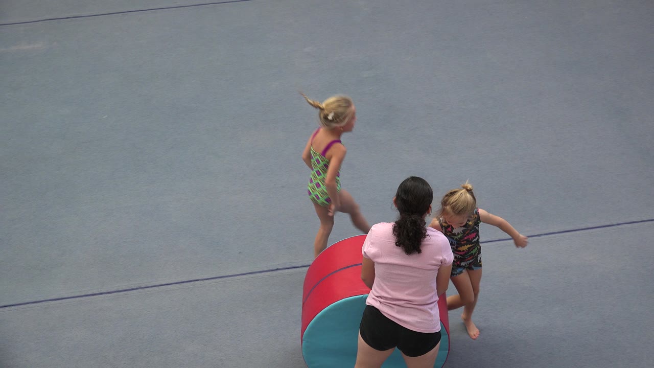 In Cabo San Lucas, Mexico, the woman remains by the red and teal barrel while one young girl steps near her and the other girl stands farther back on the gray practice floor.