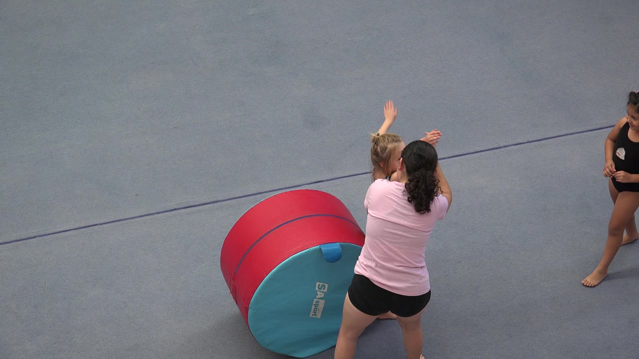 Child and instructor stand beside a foam training barrel on a gym floor.