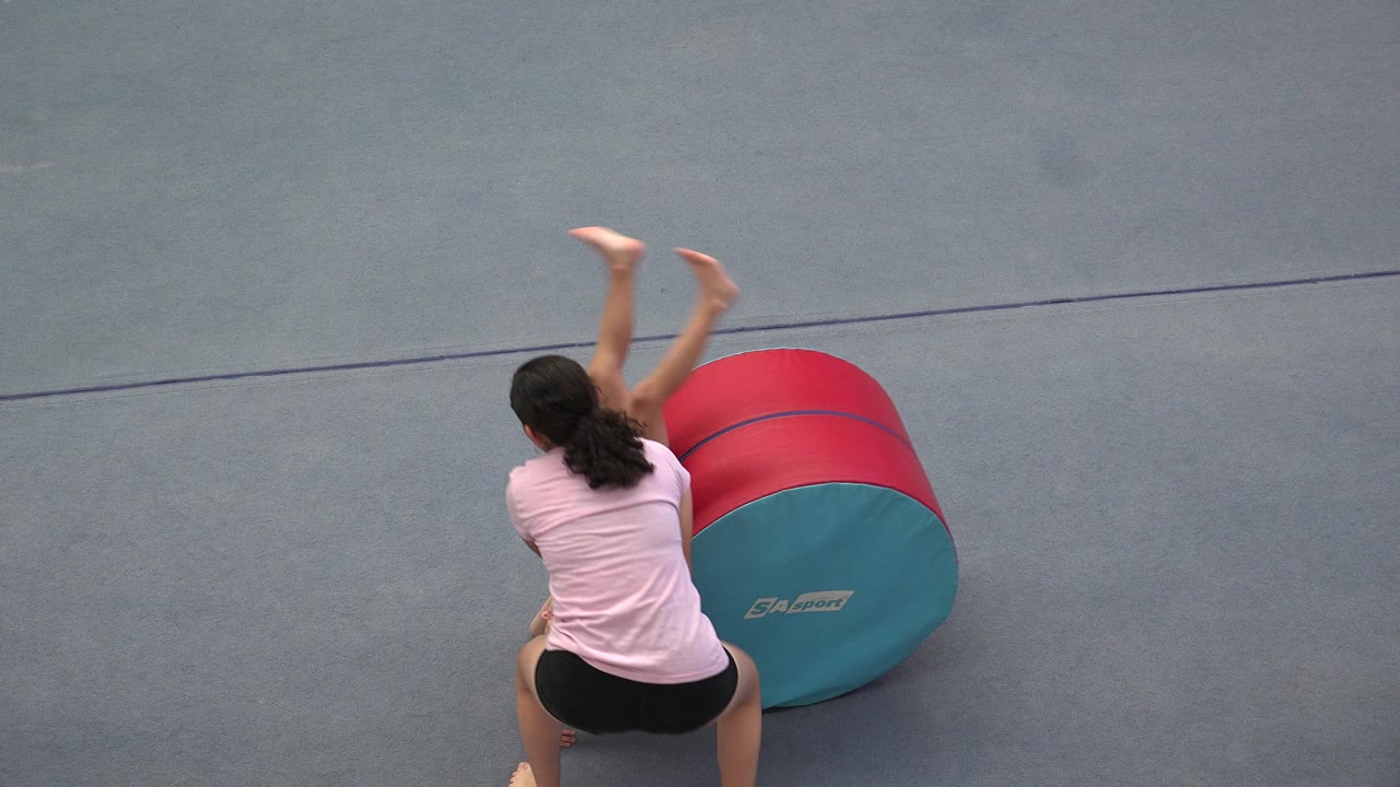 In Cabo San Lucas, Mexico, the child is inverted near the mat while the instructor faces the red and teal foam cylinder from a high angle.