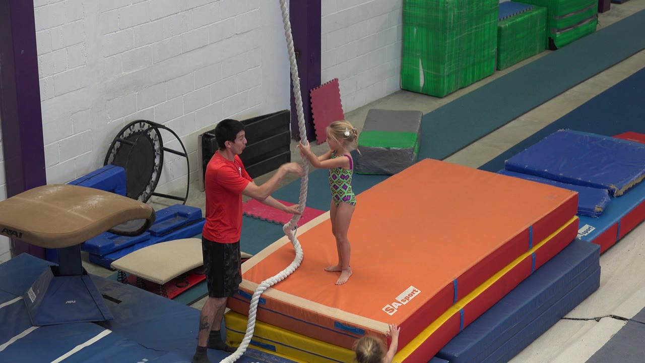 Girl and instructor beside a hanging rope in a gym
