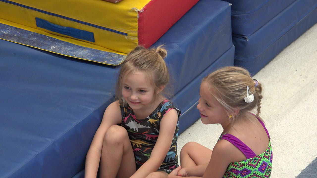 Two young girls sitting beside blue trampoline padding.