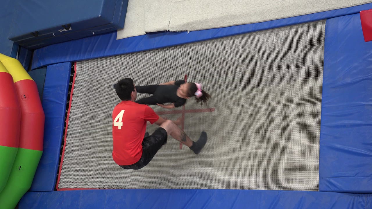 Spotter in a red shirt catches a girl over a trampoline.