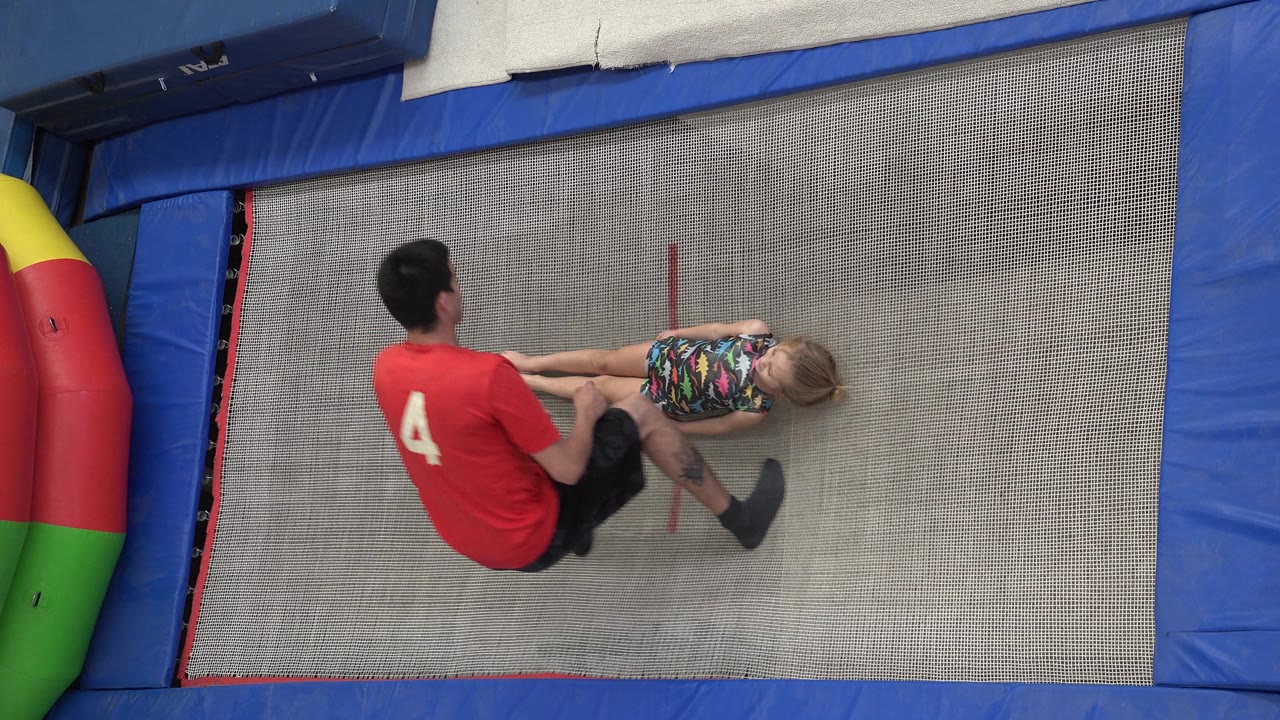 Trainer sits or crouches as the girl shifts on the trampoline.