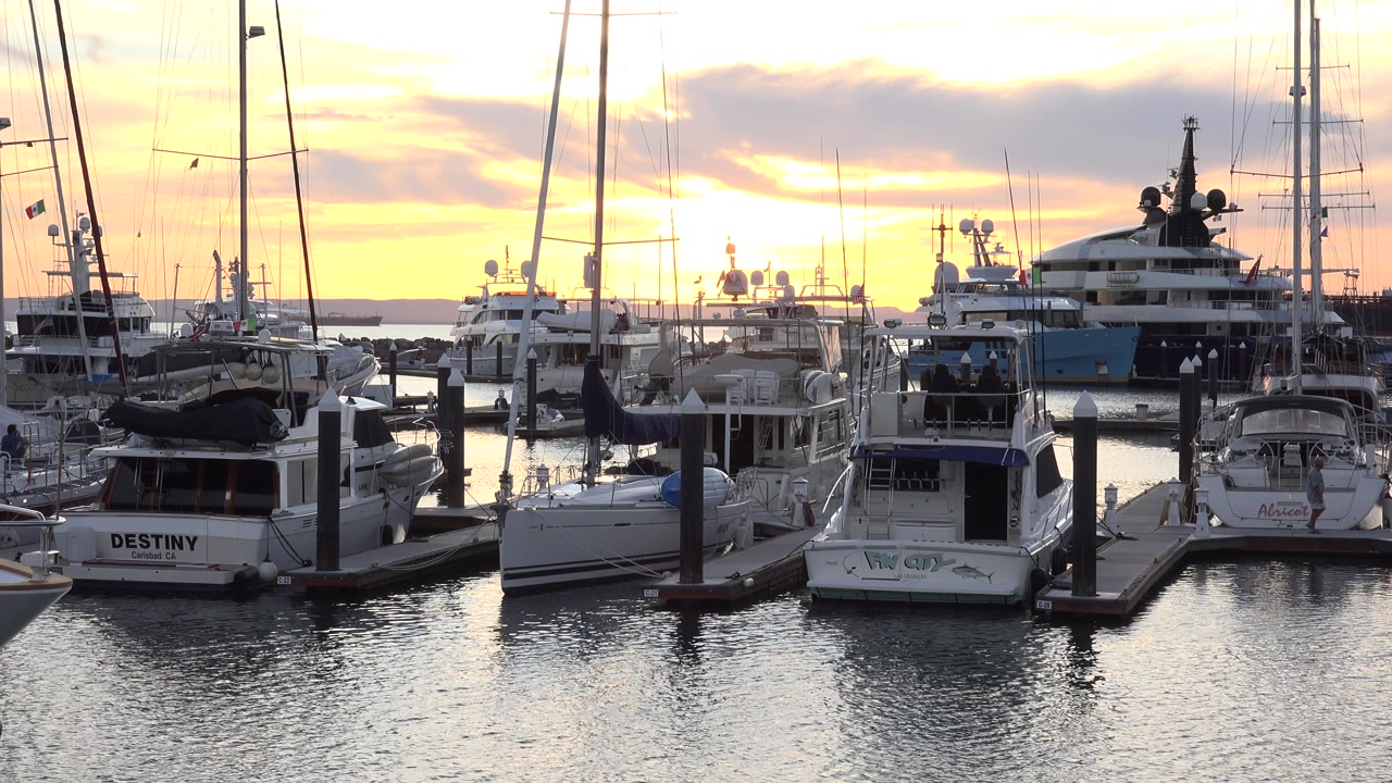 Docked boats and masts at sunset over marina water.