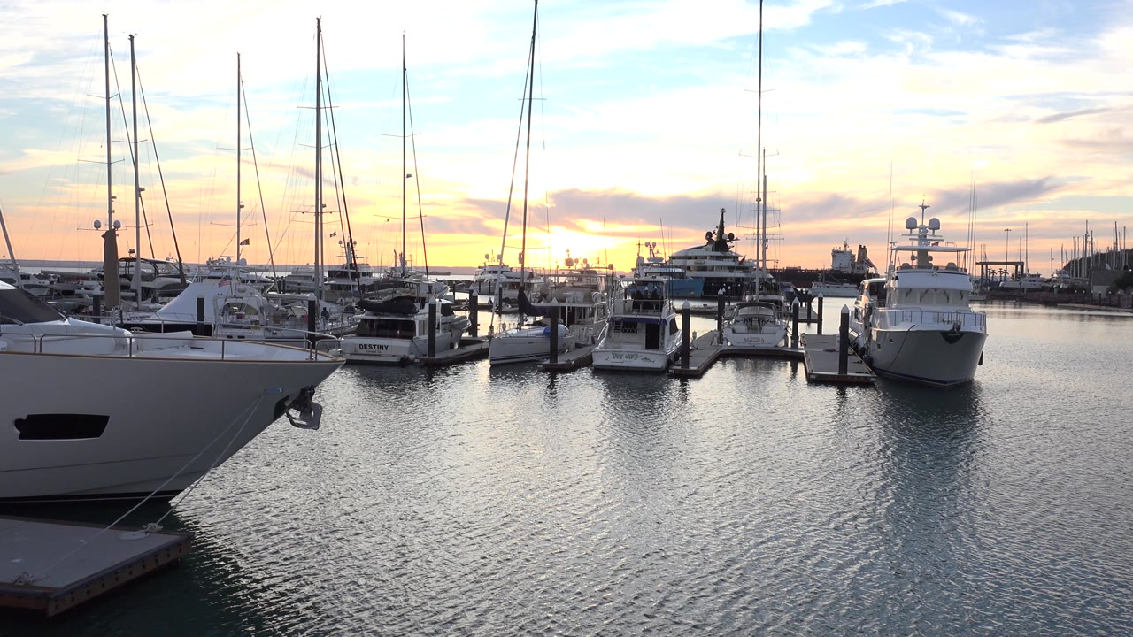 Yachts moored in a marina with sailboat masts and rippled water at sunset.